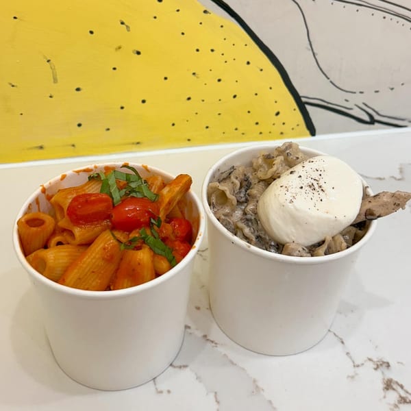 Two Pasta Lab NYC pasta cups: one with red sauce, tomatoes, and basil; the other with creamy sauce and mozzarella.