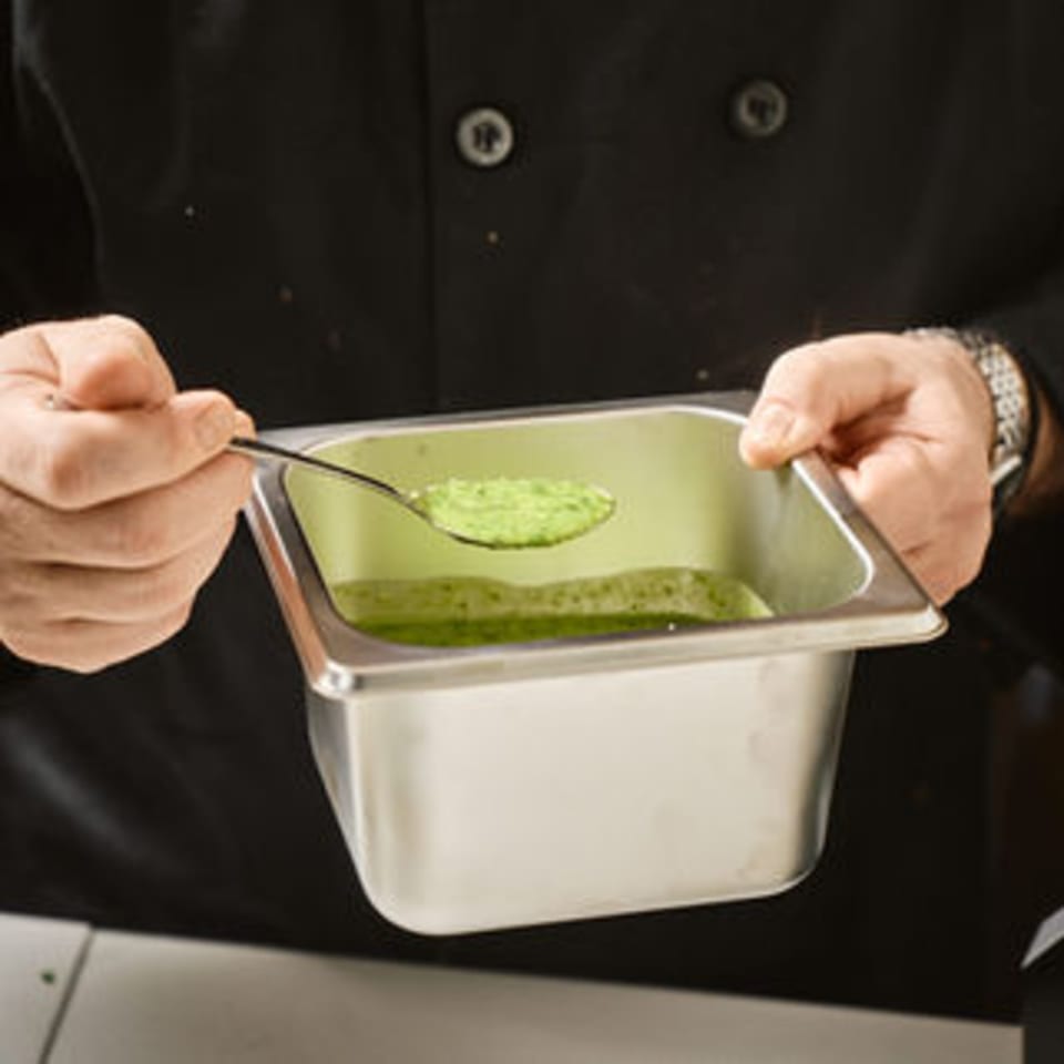 Chef's hands holding a metal container with green liquid, spooning green powder over it.