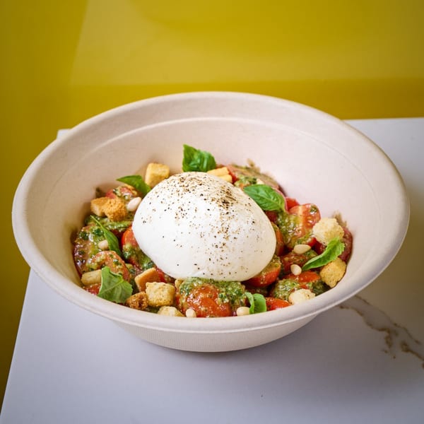 Burrata salad with cherry tomatoes, pesto, croutons, pine nuts, and basil in a bowl.