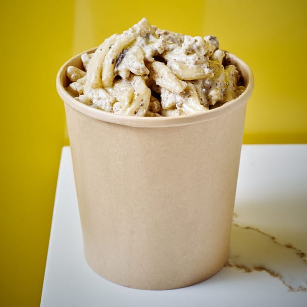 Creamy truffle pasta in a brown paper cup, against a vibrant yellow background.