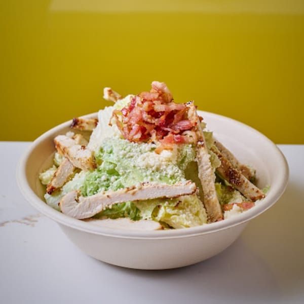 Caesar salad with grilled chicken, bacon bits, and parmesan cheese in a white bowl.